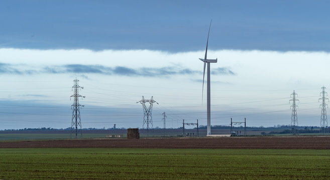 A single wind turbine in the field with electricy pylons in background