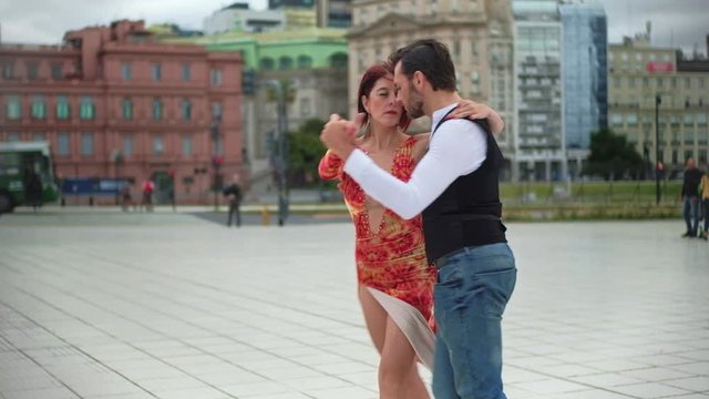 A couple of attractive tango dancers performing a suggestive routine in a square with Buenos Aires buildings in background