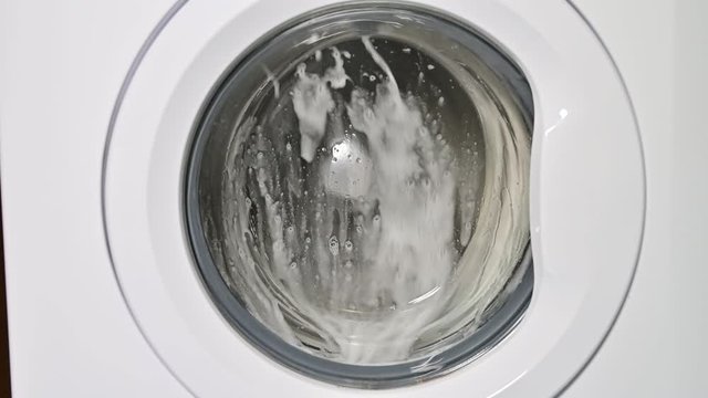 Washing machine door with rotating garments inside. focus in the center of dirty laundry and washing machine on the frame	