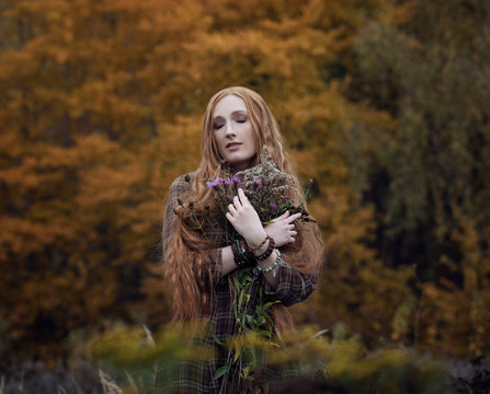 Art photo of a red-haired girl with a bouquet of autumn flowers on a background of autumn forest
