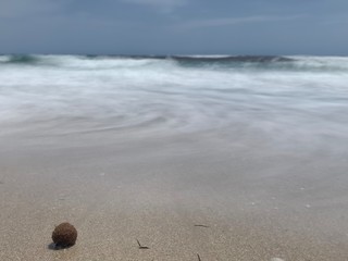 Fototapeta na wymiar Long exposure of waves on beach creating spiral pattern and algal ball