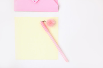 Flat lay: yellow paper, pink envelope with rhinestones, pen with pompom. Making postcard in envelope for Valentine's Day. Do it yourself. Photo from the series