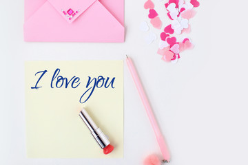 Flat lay: yellow paper, pink envelope, pen, pompom, perfume, lipstick, confetti hearts, lip print, i love you text. Making postcard in envelope for Valentine's Day.Do it yourself.Photo from the series