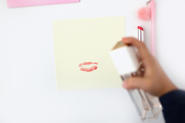 Yellow note with a red lipstick print. A bottle of pink perfume in the hand puffs on it. Making postcard in envelope for Valentine's Day. Do it yourself. Photo from the series