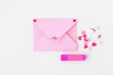 Pink envelope decorated with rhinestones, glue, confetti hearts on white background. Making postcard in envelope for Valentine's Day. Do it yourself. Photo from the series
