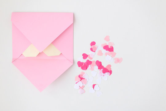 Flat lay: pink hand made envelope, confetti hearts, origami yellow heart made of paper for notes. Making postcard for Valentine's Day. Do it yourself. Photo from the series