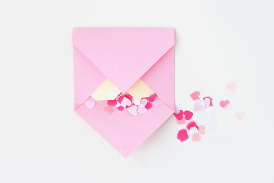 Flat lay: pink hand made envelope, confetti hearts, origami yellow heart made of paper for notes. Making postcard for Valentine's Day. Do it yourself. Photo from the series