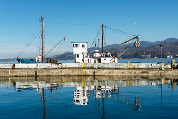 Fishing boat with a crane in a sea port. Sunny day blue sky with mountains in the background. Travel vibrant background.