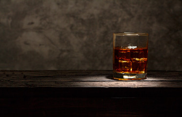 Whiskey with ice or brandy in a glass and a square carafe on an old wooden background. Whiskey with ice in a glass. Whiskey or cognac. Selective focus.