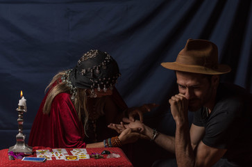 Obraz premium Gypsy fortuneteller or esoteric Oracle reading hand lines in a young man with hat