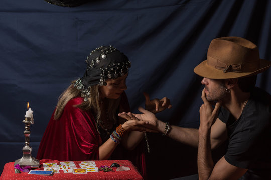 Gypsy fortuneteller or esoteric Oracle reading hand lines in a young man with hat