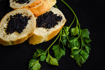 three tasty sandwiches with black caviar with green parsley on the dark background