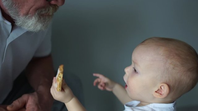 Little grandson feeds his grandfather with cookies. Close portrait, good grandfather, happy family