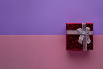 Red gift box with silver bow on two-tone pink and blue paper background top view with copy space. Can be used for Valentines day, birthday, March 8, holiday greetings banner.