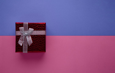 Red gift box with silver bow on two-tone trendy pink and blue paper banner top view with copy space. Valentines day, birthday, March 8, greetings banner, for discounts, sale template.
