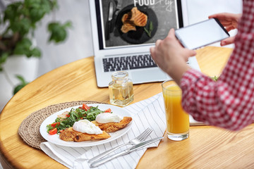 Food blogger taking photo of her lunch at wooden table indoors, closeup