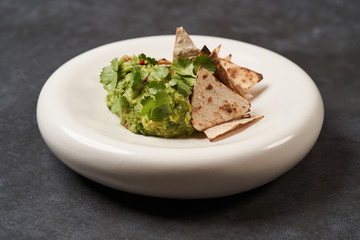 Guacamole with pita chips on white plate, close-up. Mexican guacamole