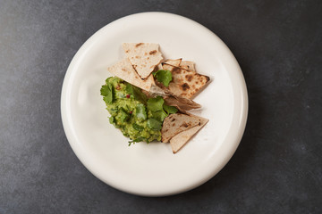 Guacamole with pita chips on white plate, close-up. Mexican guacamole