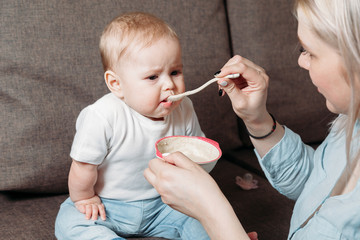 young mother feeds her son with a spoon of fruit puree