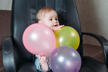 Obraz premium funny child sitting on chair little boy having fun playing big colored balloons