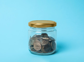 Glass jar with coins on light blue background