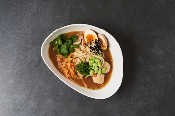 Ramen noodle soup with chicken, shiitake mushroms and egg in a white bowl, top view