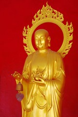 Fototapeta premium Golden buddha against a red wall at a temple in Phuket, Thailand.