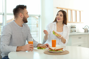 Happy couple having breakfast with sandwiches at table in kitchen