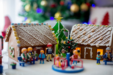 Cute gingerbread houses, made by kids, decorated with toys, trees and playground on table