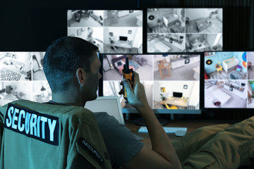 Security guard with portable transmitter monitoring modern CCTV cameras indoors