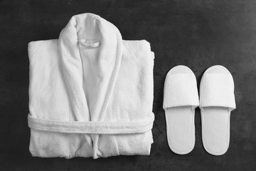 Clean folded bathrobe and slippers on black stone background, flat lay - obrazy, fototapety, plakaty