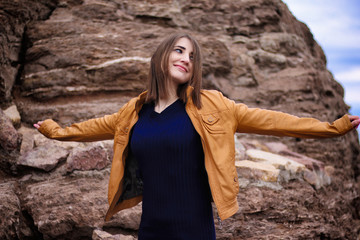 Image of happy girl in yellow jacket smiling while sitting by rock in morning