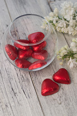 Composition Valentine's Day. Red chocolate hearts and a branch of white lilac on a wooden vertical background.