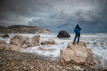 Obraz premium Unrecognised person standing at the rock and enjoying the stormy seascape