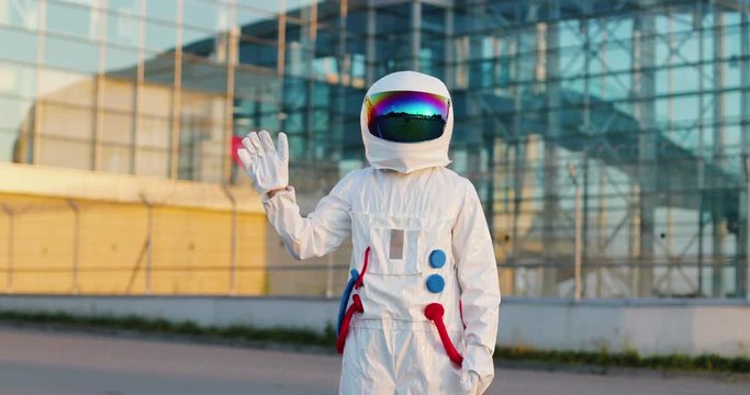 Astronaut in the full space costume with head armor standing outside, waving hand and getting ready to fly in cosmos.