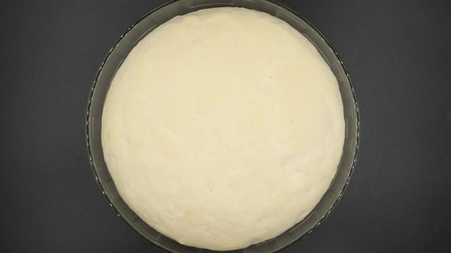 Yeast dough rising in glass bowl on black background, top view.