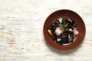 Obraz na płótnie Canvas Delicious black risotto with seafood on white wooden table, top view. Space for text