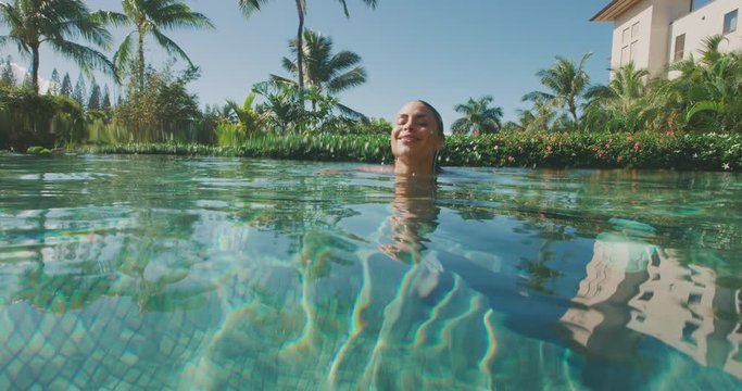 Attractive woman swimming underwater in a resort swimming pool and coming up the the surface smiling, happy woman on vacation