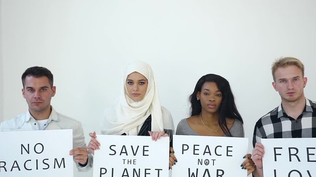 Attractive picture of four serious multiethnic young people which posing on camera with posters with written words"Free love.Peace not war.Save the planet.No racism"