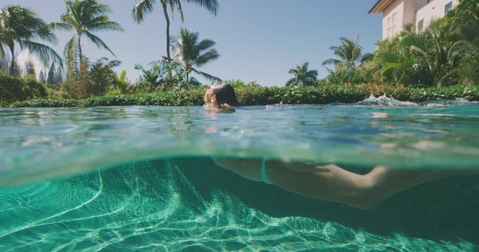 Under over shot of an attractive woman swimming in a tropical swimming pool underwater, awesome island vacation