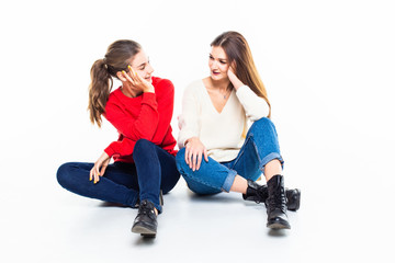 Two teen girl friends have fun sitting on the floor isolated on white background