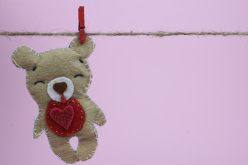 Bear handmade felt hanging on a clothesline, pink background, space for text. Valentine's day