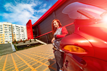 Beautiful brave woman is leaning on her motobike near modern building. Red haired girl. Speed and fashion concept.