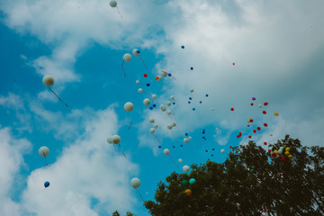 Multicolored balloons pile soaring into the blue sky with white clouds.
