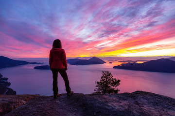 Adventurous Caucasian Girl standing on top of a mountain during a colorful winter sunset. Taken on Tunnel Bluffs Hike, North of Vancouver, BC, Canada.