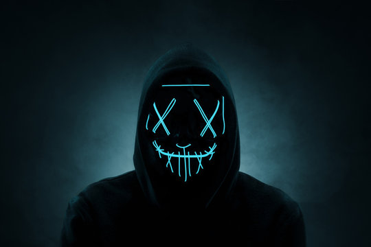 Portrait of an anonymous man, hacker wearing neon mask over dark background