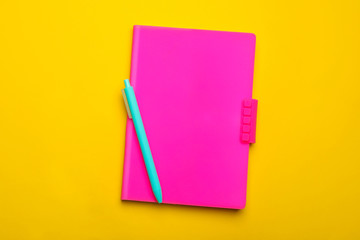 Pink notebook and pen on yellow background, top view