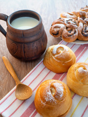 On the towel are fresh soft buns and a wooden spoon. A large mug of milk on the table.