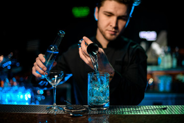 Professional bartender pouring a blue alcoholic liquor from the jigger to a glass measuring cup