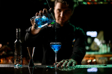 Bartender pouring a alcoholic drink from the measuring cup to the glass through the strainer filter